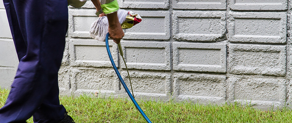 A professional pest control expert applying a pest control solution to the perimeter of a residential property in The Villages, FL.