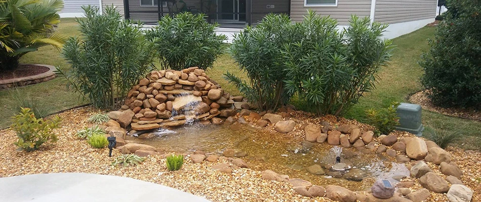 A fountain and landscaping with new rocks and a plam tree, lawn and house in the background in The Villages, FL.
